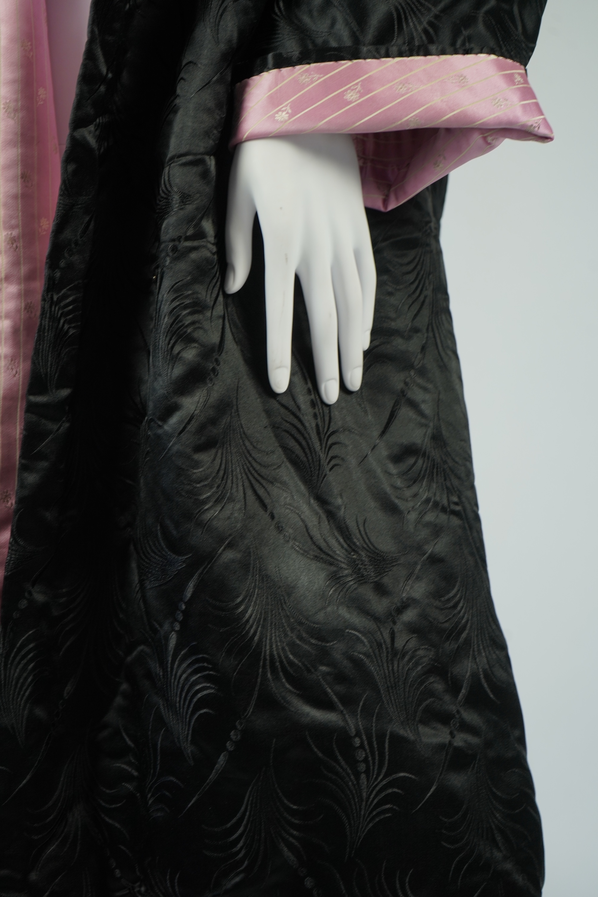 A 20th century ladies black silk damask opera coat, trimmed with a white fur collar and pink silk stripe brocade lining. 116cm from shoulder to hem. Condition - seams unstitched in places, small nick to black brocade by